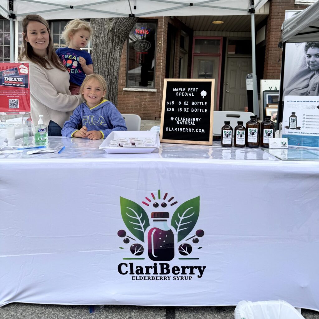Mother and two daughters standing behind a market stand for clariberry elderberry syrup.